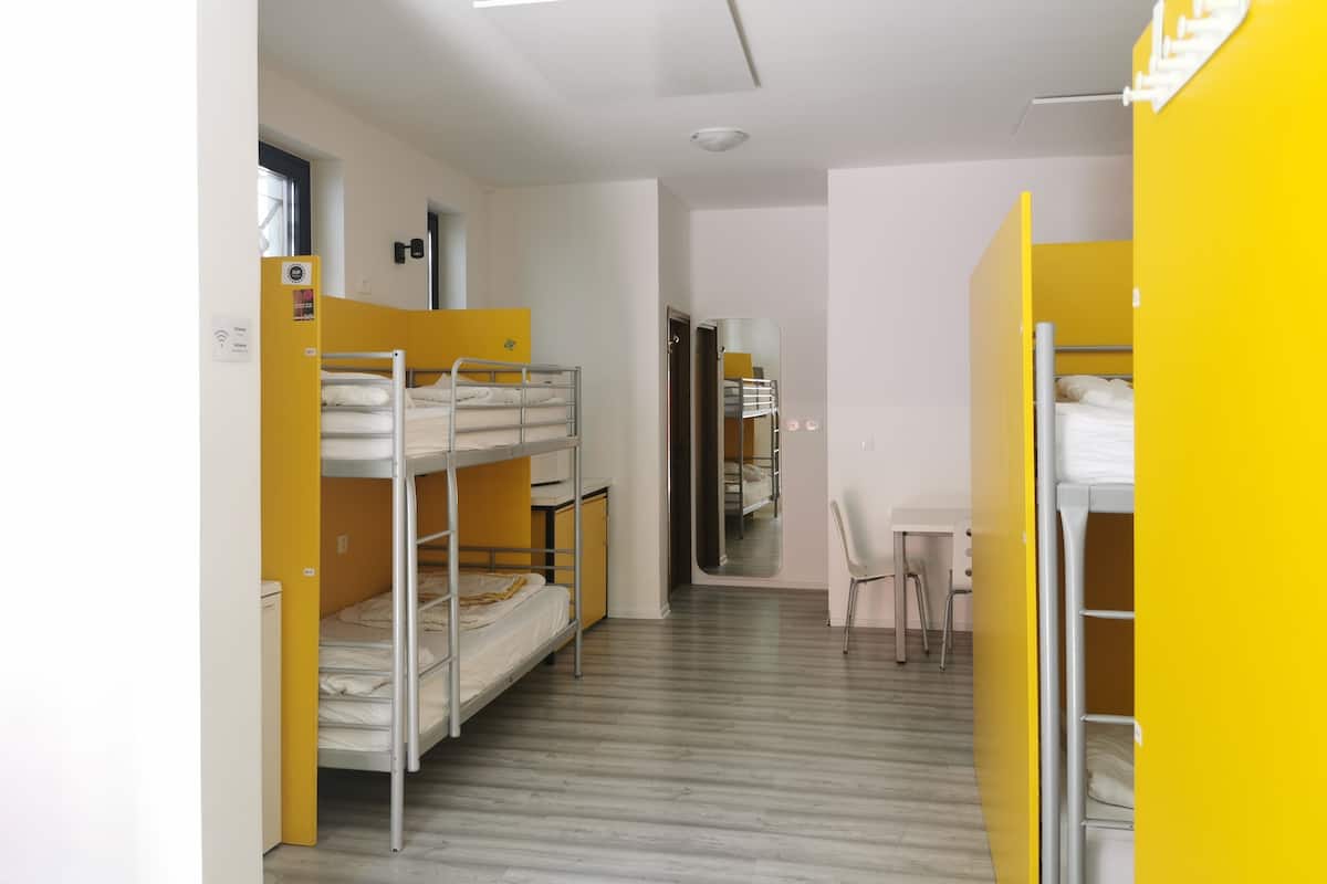 A dormitory room with bunk beds, a desk, and a chair.