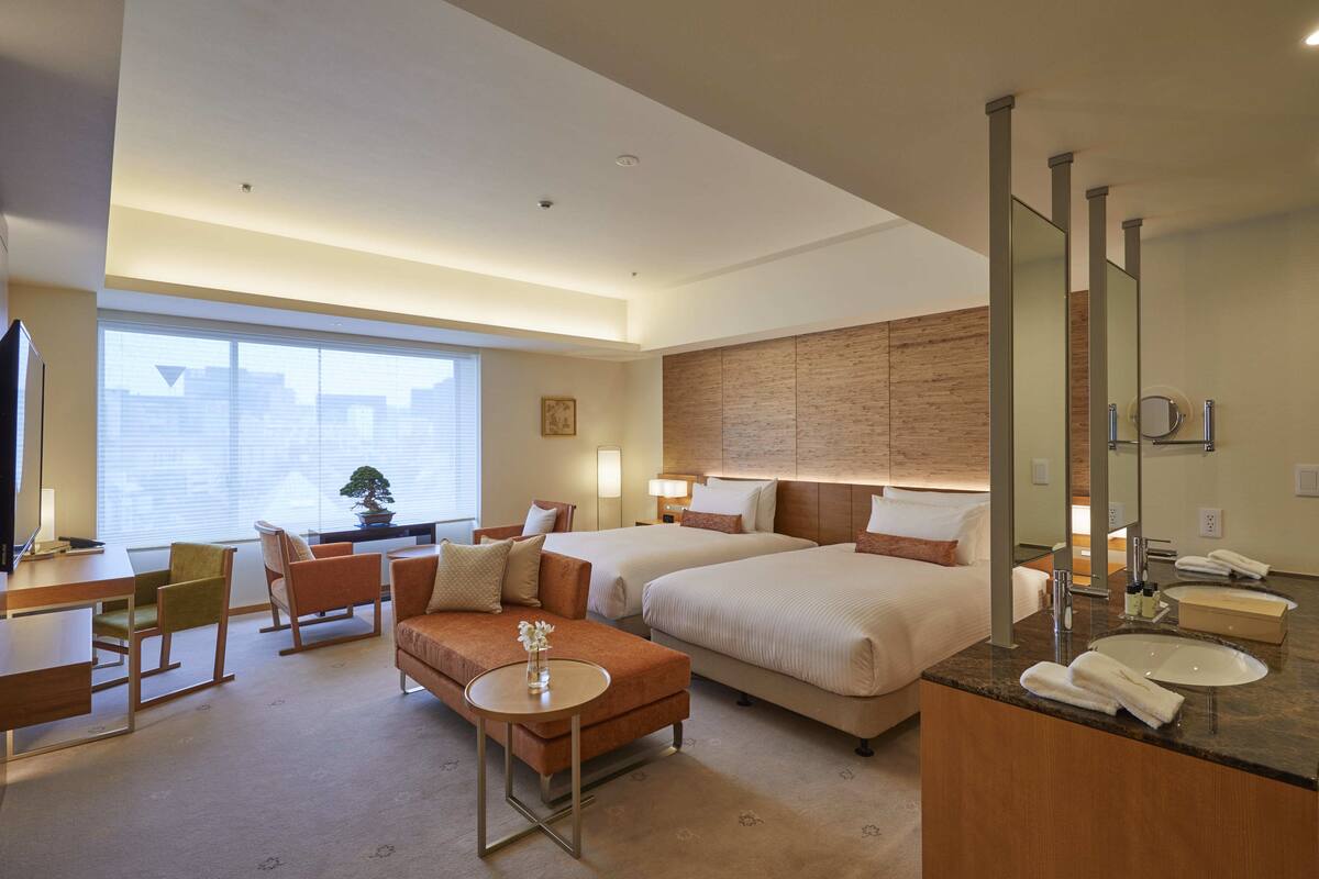 Habitación de hotel con dos camas, un sofá, un escritorio y un baño con un espejo grande y lavamanos.