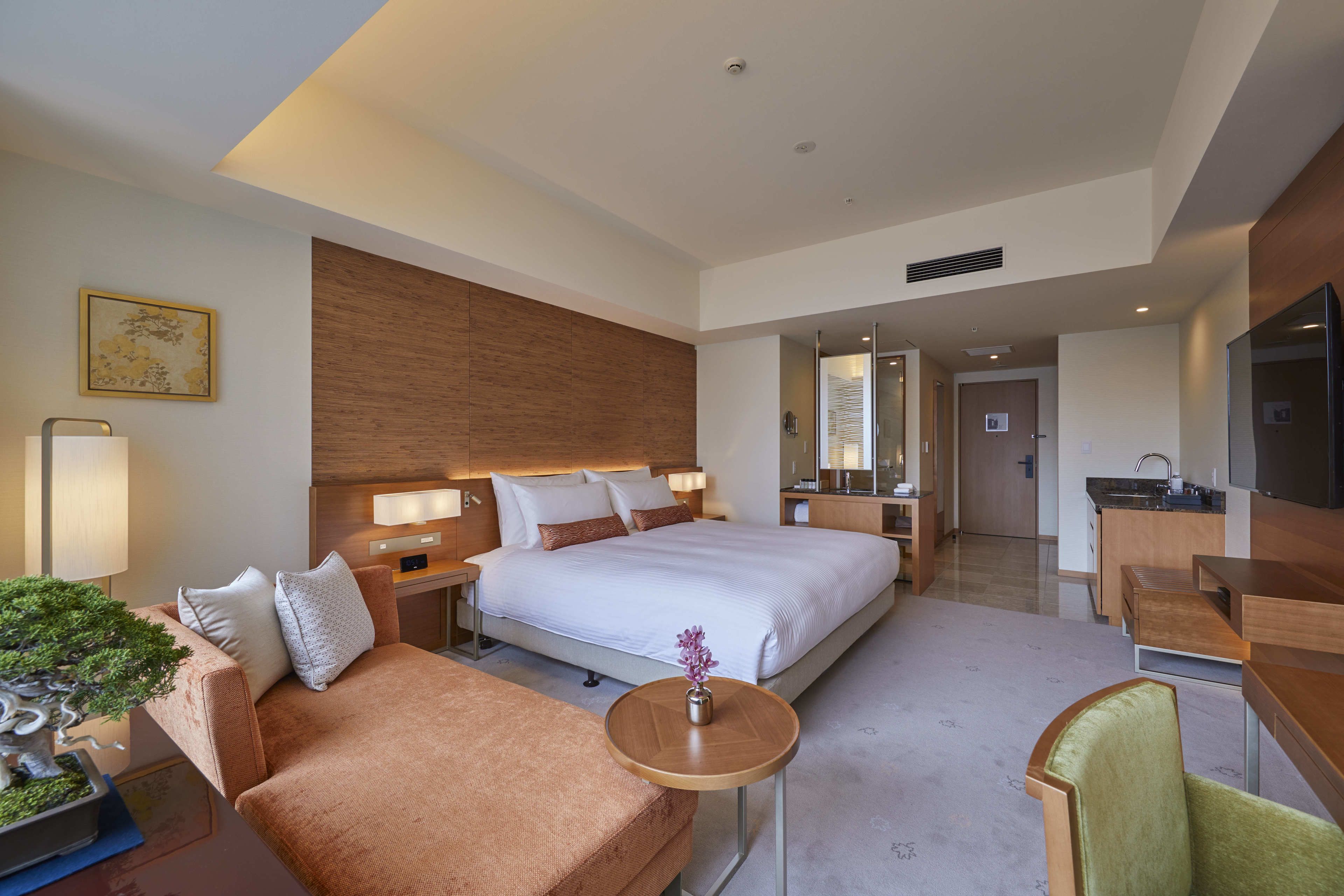Une chambre d’hôtel moderne avec un grand lit, un canapé, une petite table avec un vase, un bureau et une télévision.