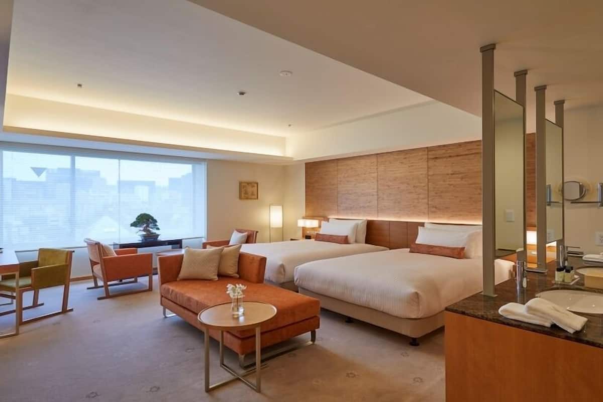 Habitación de hotel con dos camas, un escritorio, un sofá, una mesita y un baño con espejo y lavamanos.