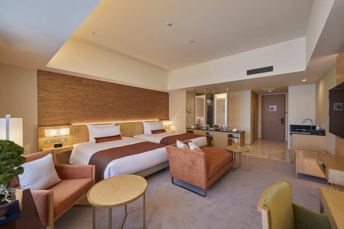 Una habitación de hotel moderna con una cama grande, un sofá, una mesita y una kitchenette.