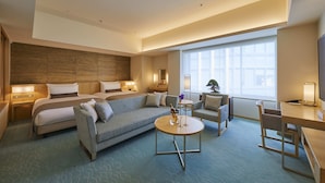Een moderne hotelkamer met een groot bed, een bank, een bureau en een stoel. Een groot raam zorgt voor natuurlijk licht.