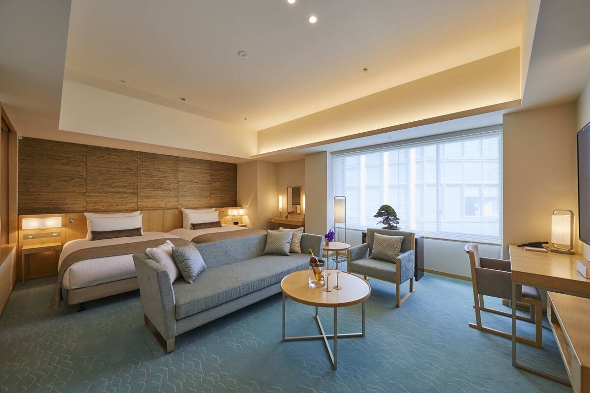 Habitación de hotel moderna con una cama grande, un sofá, un escritorio y una silla. Un ventanal grande proporciona luz natural.