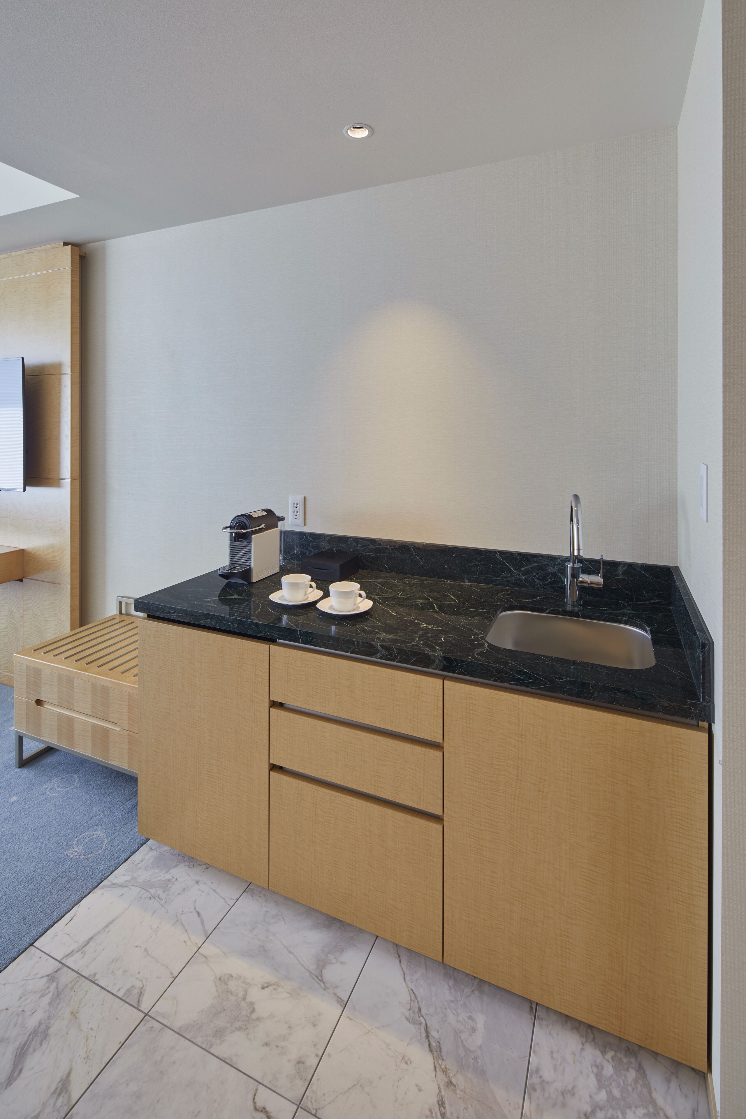 A modern kitchen with a black marble countertop, stainless steel sink, and wooden cabinets.