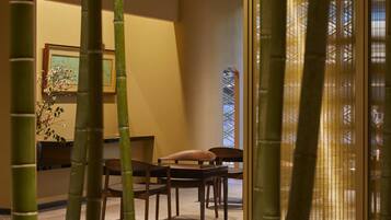 Una habitación con una mesa y sillas de madera, un cuadro enmarcado en la pared y una ventana con un diseño geométrico.