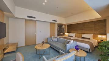 A modern hotel room with a large bed, a sofa, two small tables, and a TV.