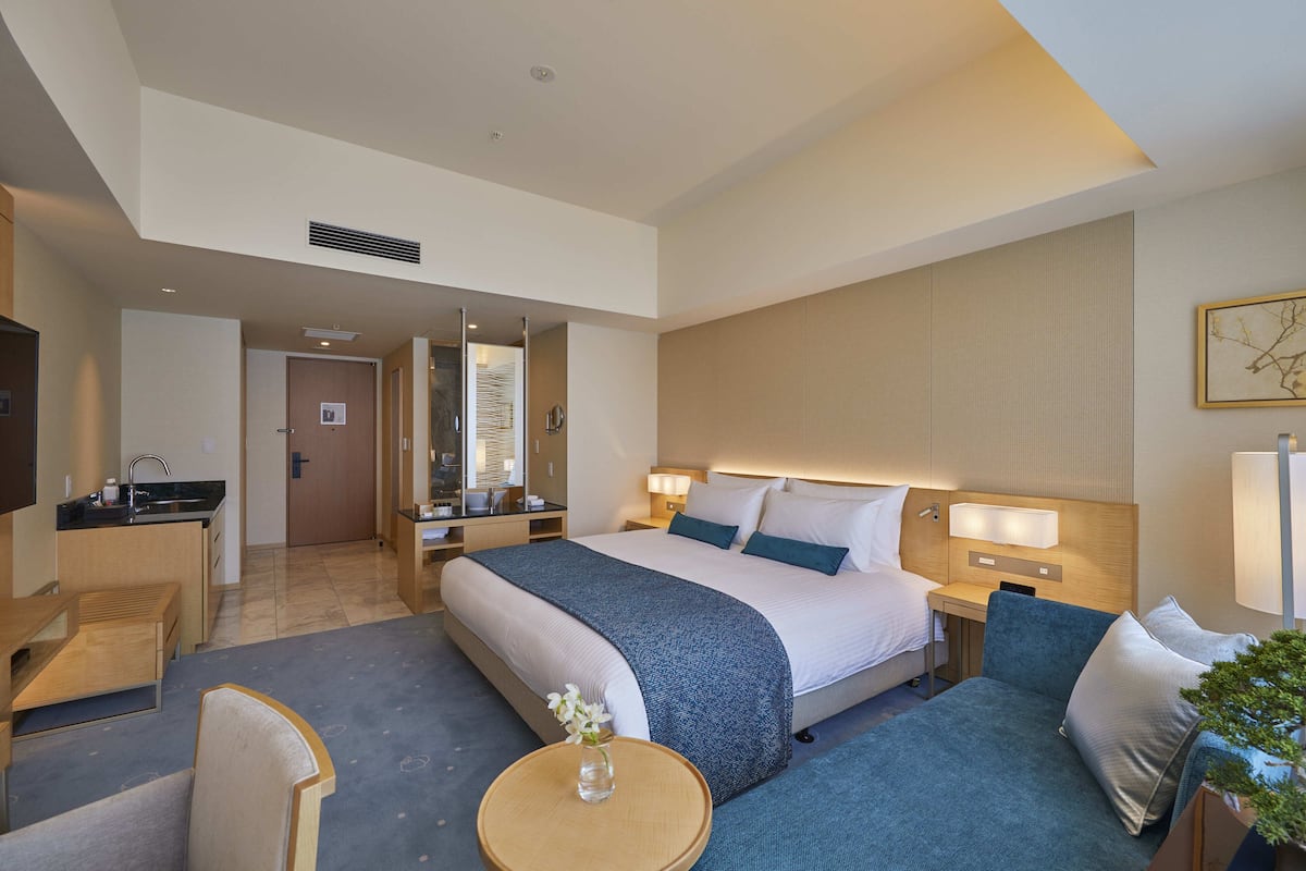 Una habitación de hotel con cama, mesitas de noche, escritorio, silla y una pequeña mesa con un florero.