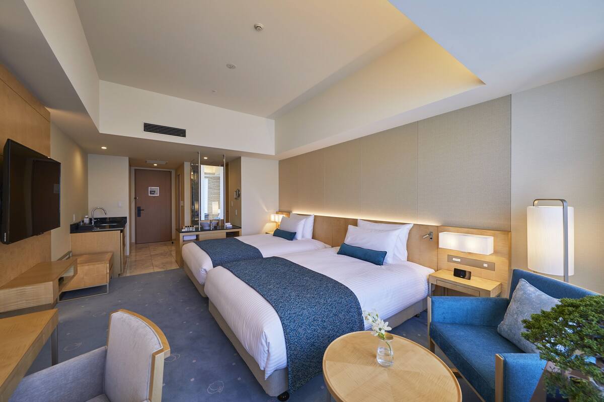Habitación de hotel con una cama grande, un sofá, un escritorio, un televisor y un baño visible a través de una puerta abierta.