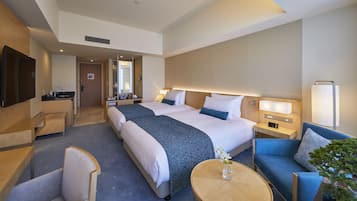 Habitación de hotel con una cama grande, un sofá, un escritorio, un televisor y un baño visible a través de una puerta abierta.