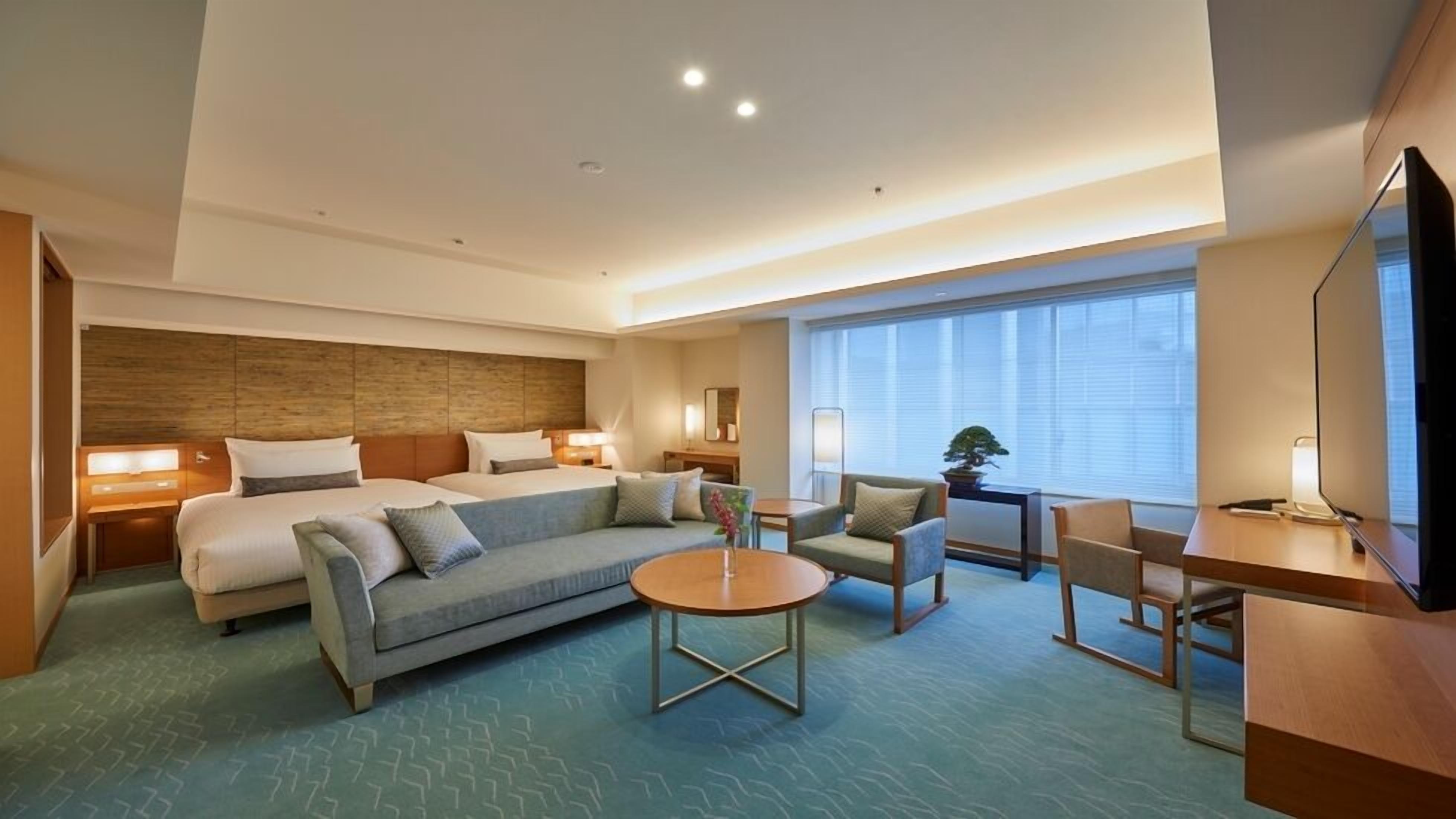 A hotel room with a bed, sofa, armchair, small table, and a TV.