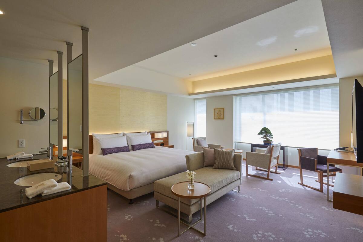 Una habitación de hotel moderna con una cama grande, un sofá, un escritorio y un baño con espejo y lavabo.