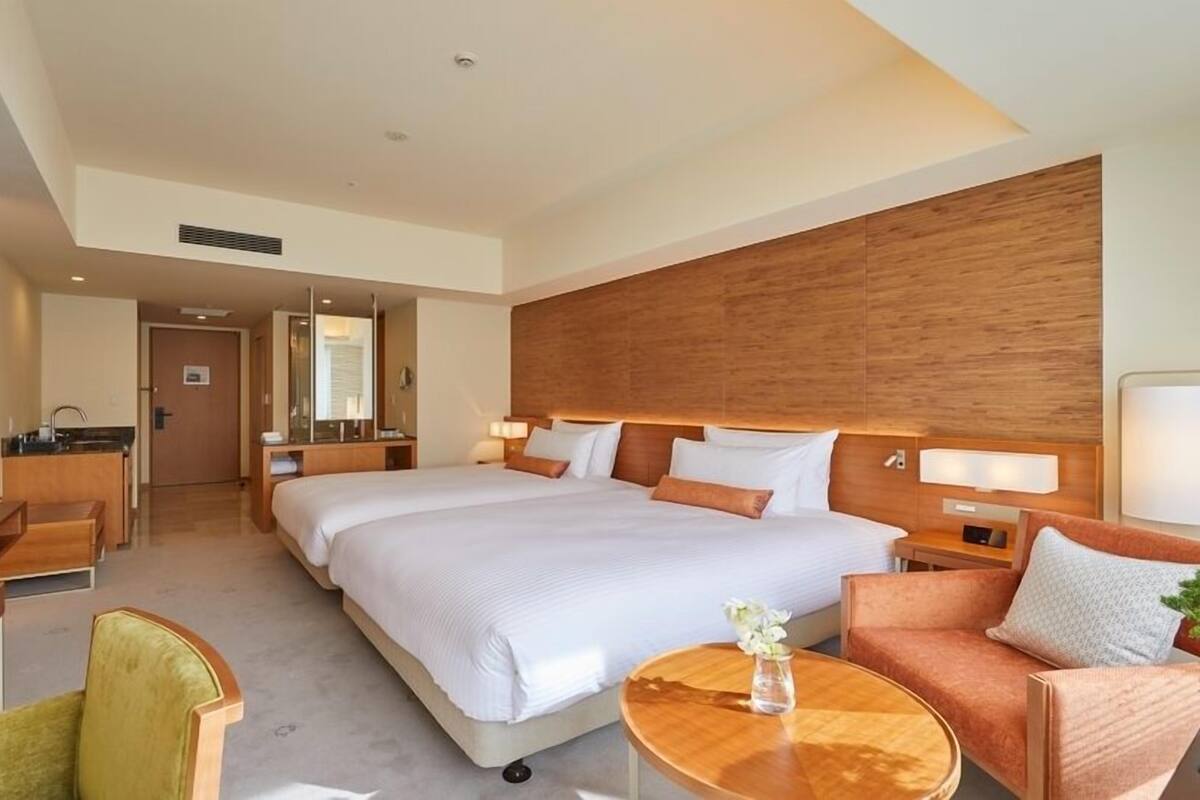 Habitación de hotel con una cama grande, un escritorio, una silla, un sofá, un televisor y una mesita de noche con un florero.