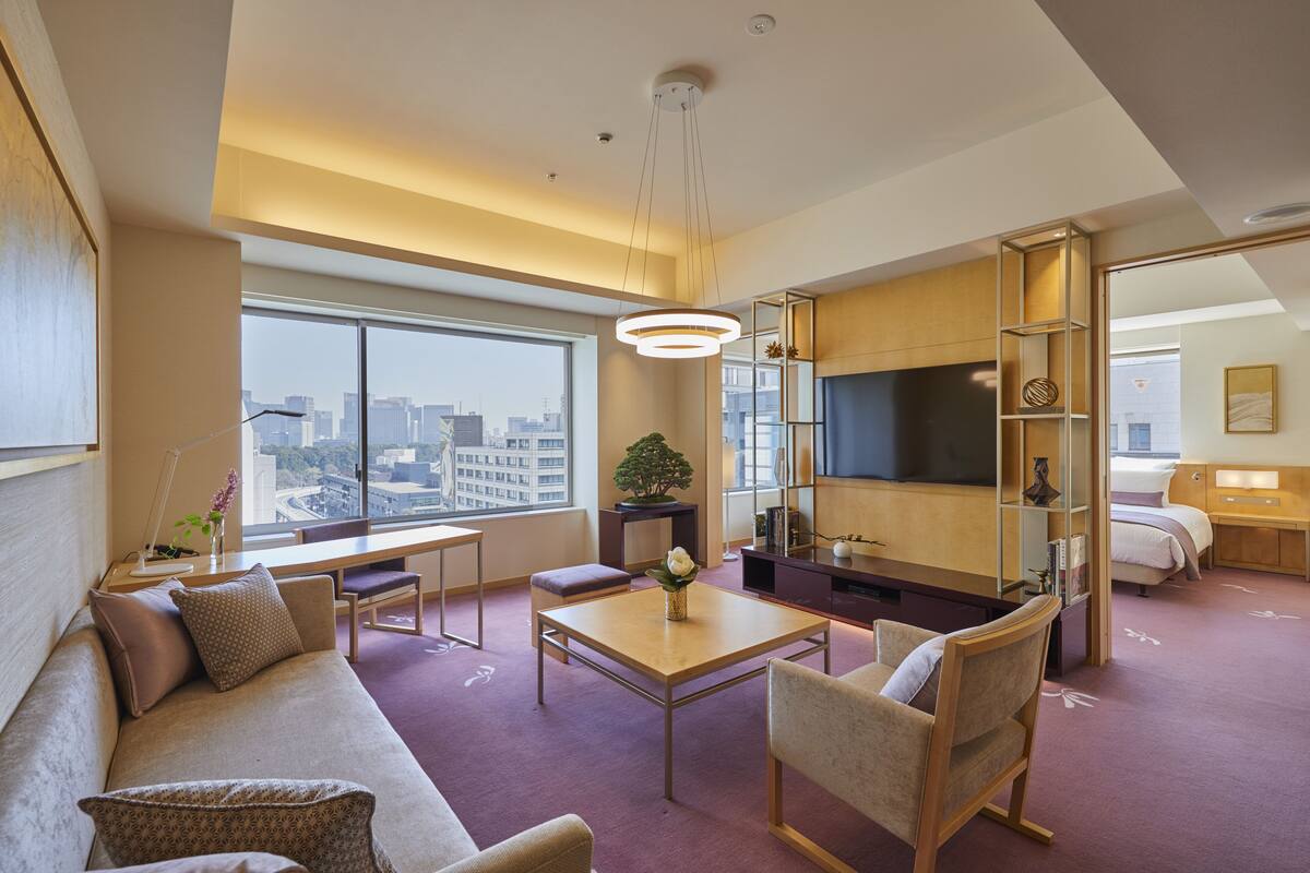 Una habitación de hotel moderna con un ventanal grande, un sofá, una mesita de centro, un televisor y una cama.