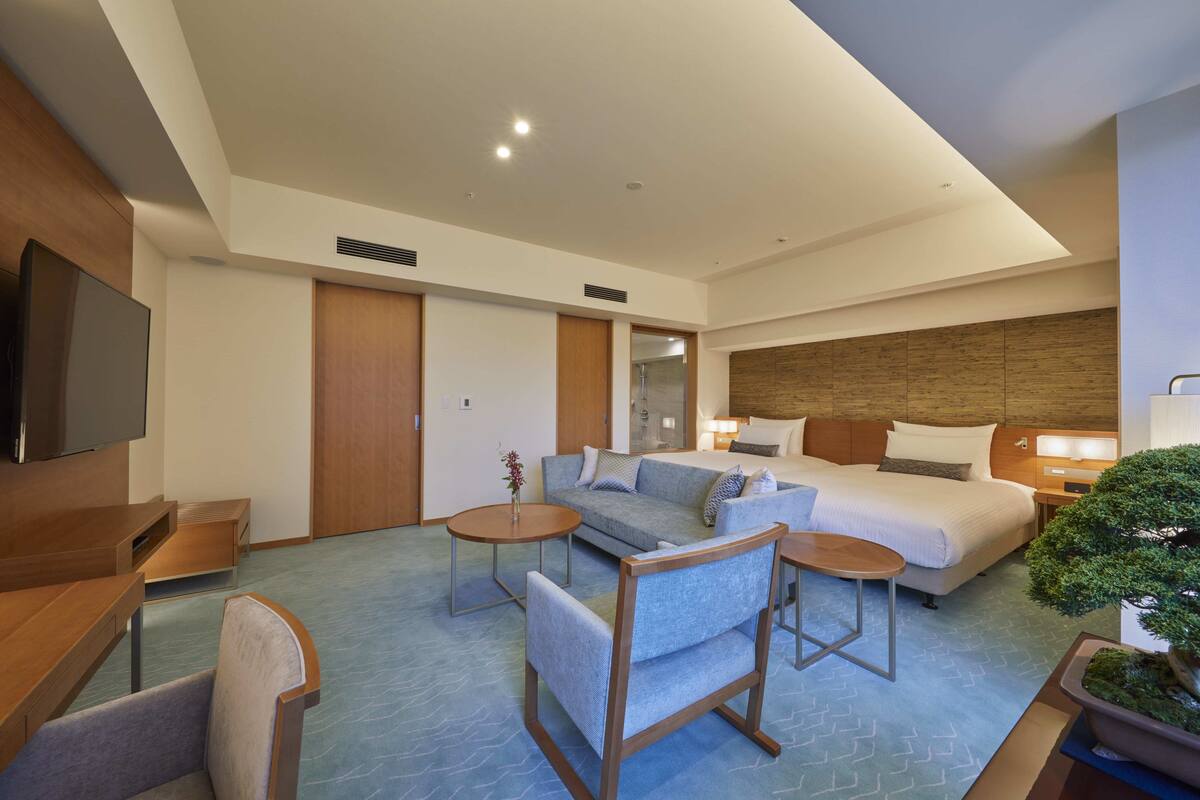 Una habitación de hotel con cama, sofá, televisión, escritorio y una planta pequeña.
