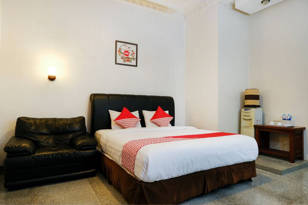 Une chambre d’hôtel avec un lit, un canapé en cuir noir, une petite table avec une lampe et un radiateur fixé au mur.