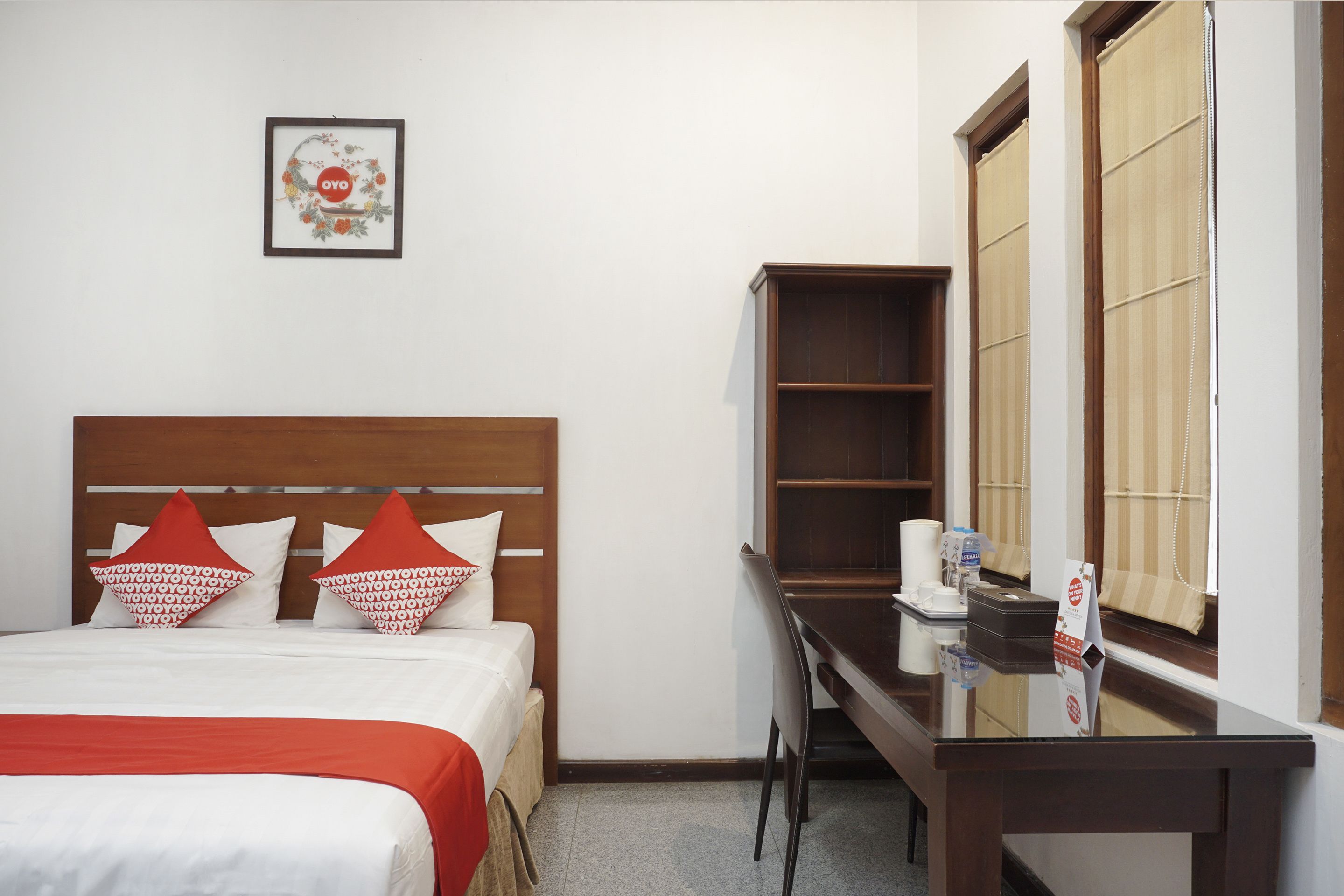 Een hotelkamer met een bed, een bureau, een telefoon en een raam met luxaflex.
