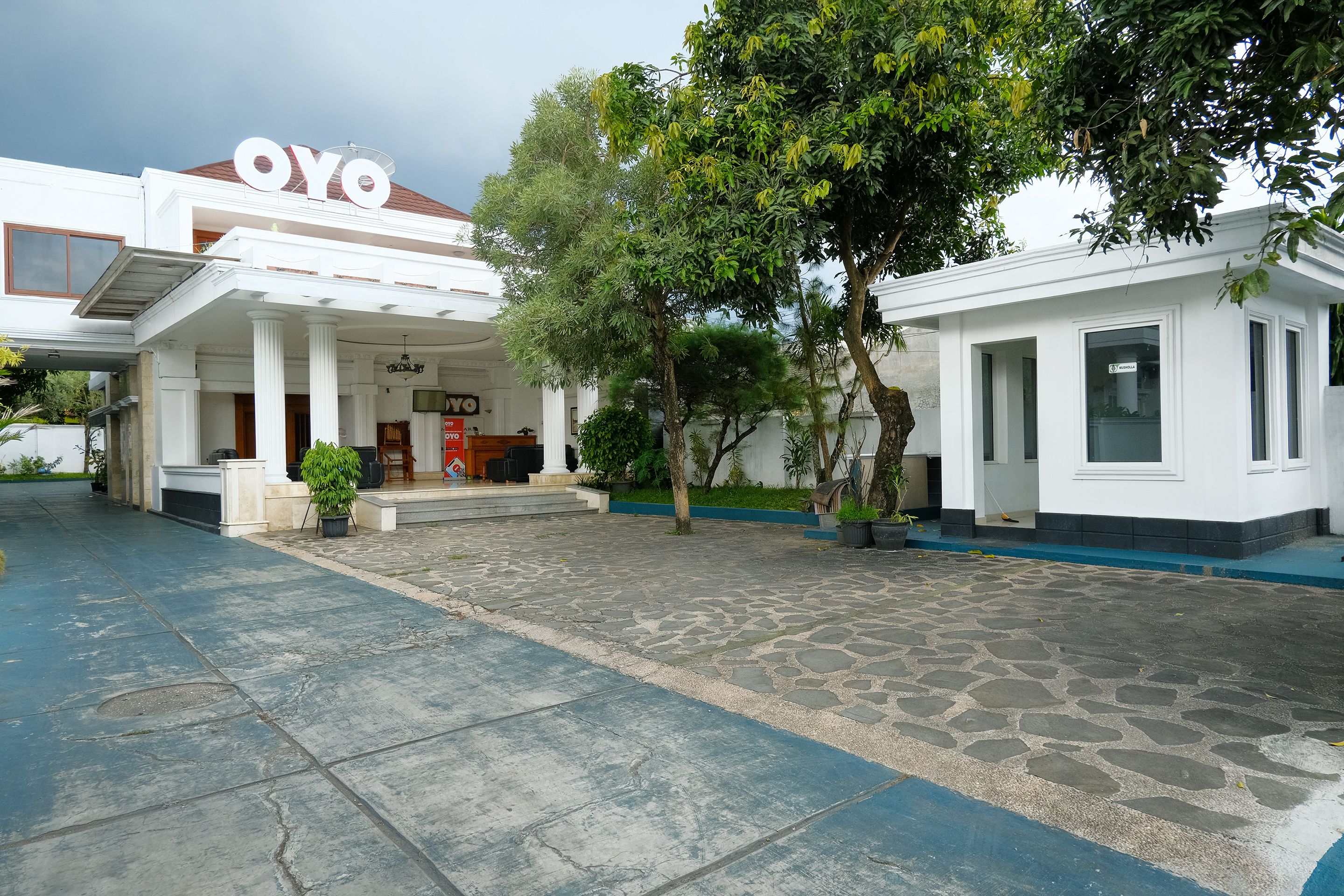 A hotel with a prominent 'OYO' sign, a covered entrance, and a paved courtyard with trees.