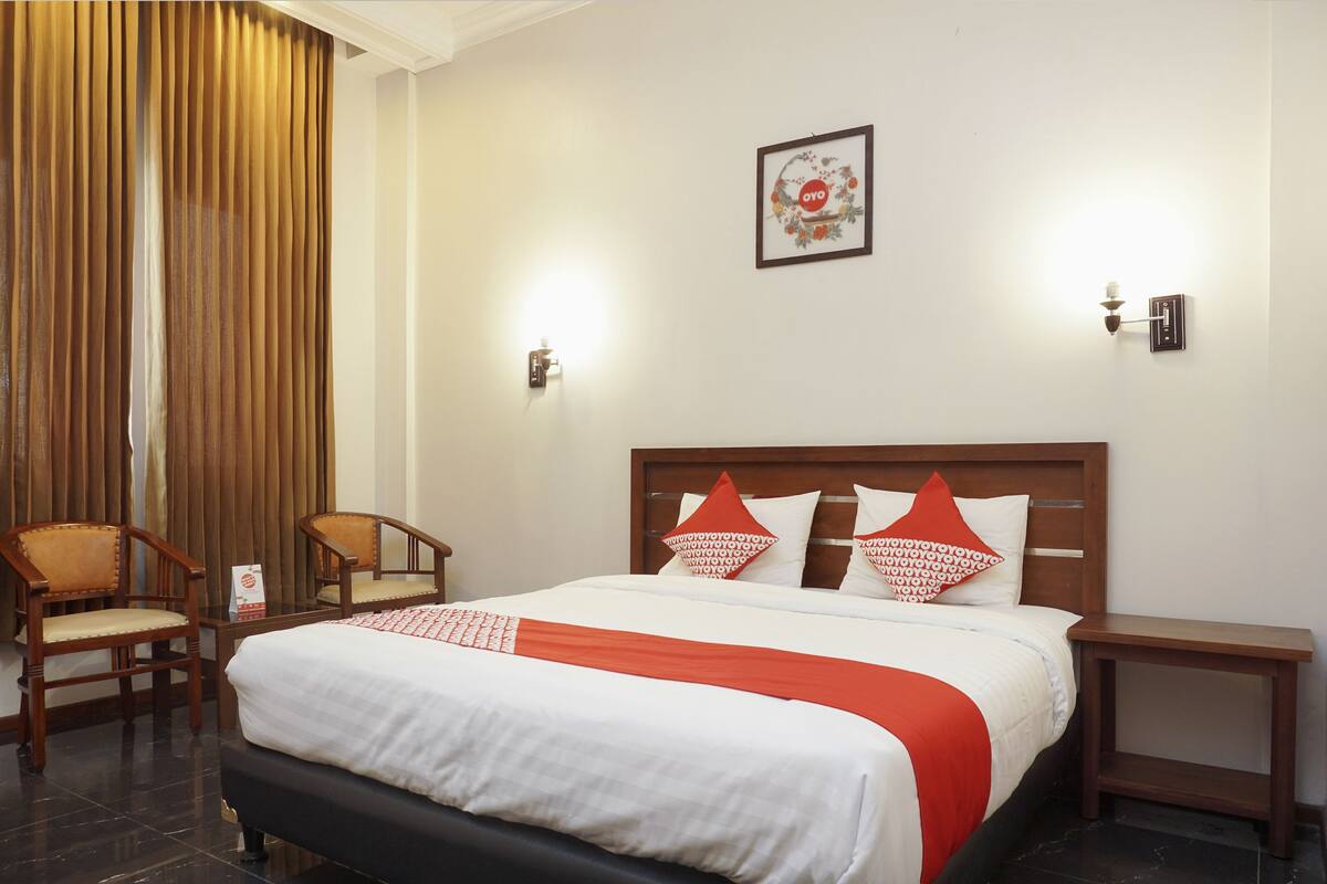 Une chambre d’hôtel comprenant un lit, deux chaises, une table de chevet et un luminaire fixé au mur.