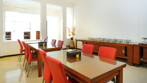 A conference room with a glass table, red chairs, a vase with flowers, and a wooden cabinet with kitchenware. - Super OYO OYO Capital O 514 Omah Pari Boutique Hotel (Yogyakarta)