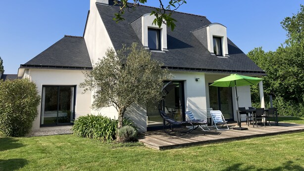 A modern house with a sloped roof, large windows, and a patio with outdoor furniture. - House near the sea (500 m) (Le Tour-du-Parc)
