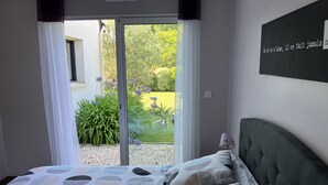 A bedroom with a bed, a window with curtains, and a view of greenery outside. - House near the sea (500 m) (Le Tour-du-Parc)