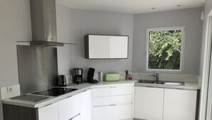 A modern kitchen with white cabinets, a stainless steel range hood, a built-in sink, and a window with a view of greenery. - House near the sea (500 m) (Le Tour-du-Parc)