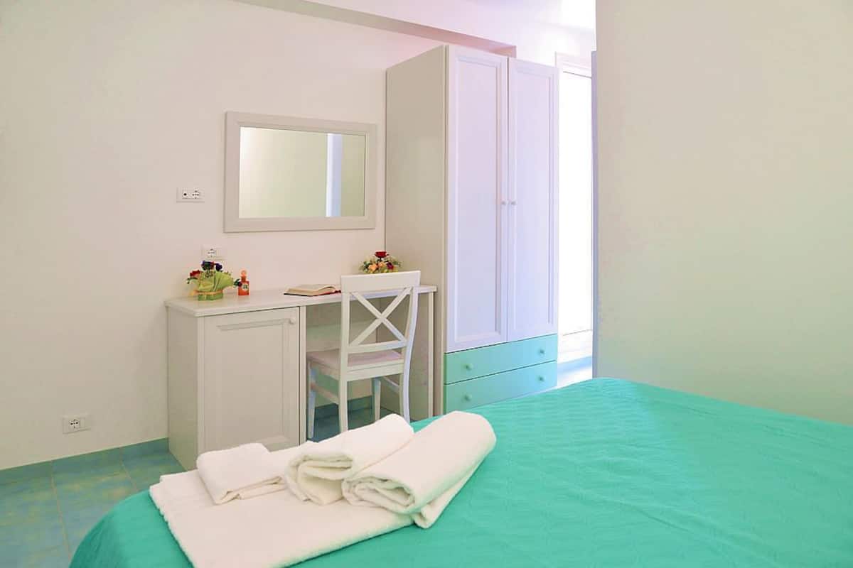 A bedroom with a bed, a desk with a chair, a wardrobe, and a mirror on the wall.