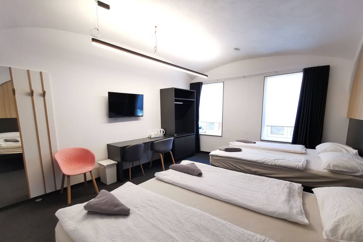 A hotel room with two beds, a desk, a chair, a TV, and a wardrobe.