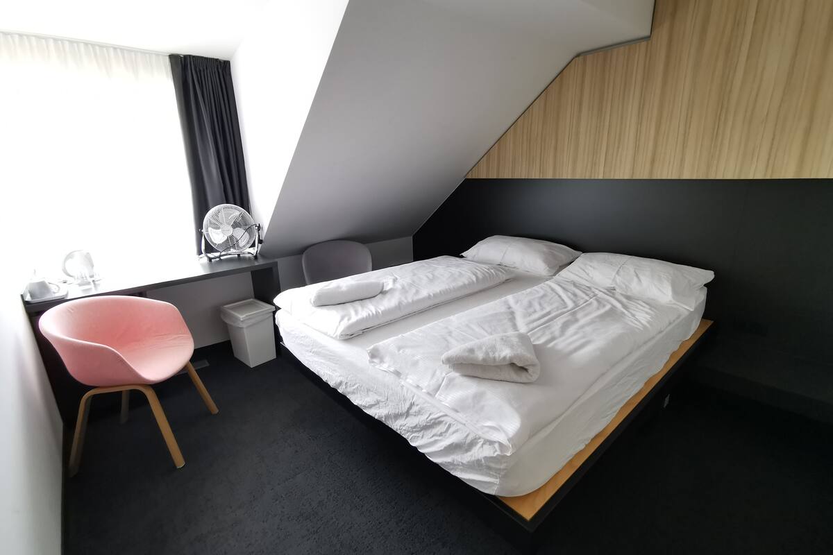 A modern hotel room with a bed, a desk, a chair, and a window with curtains.