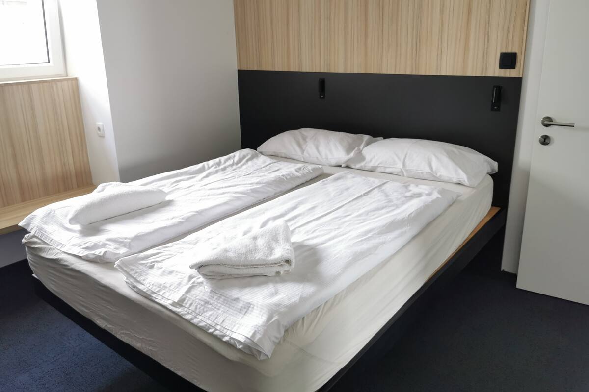 A bed with white linens and a folded towel, a wooden headboard, and a door with a handle.