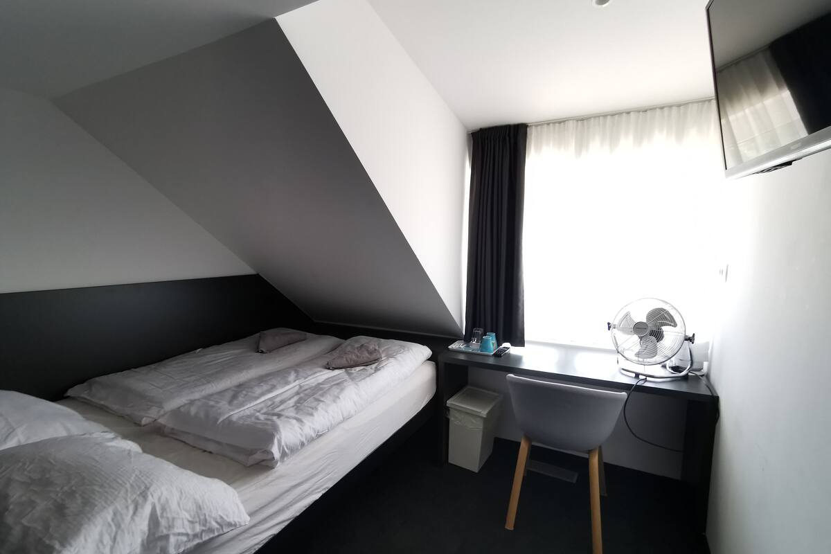 A modern hotel room with a bed, a desk, and a chair.