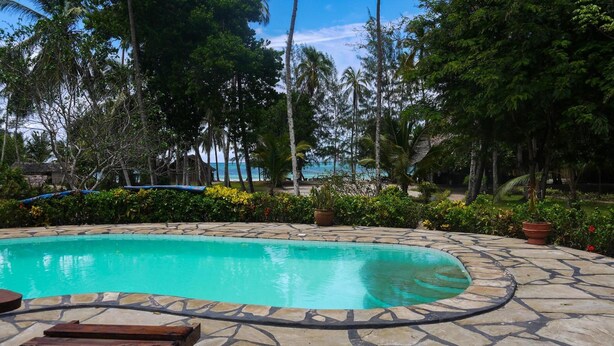 A pool surrounded by tropical vegetation and a view of the ocean. - Bidi Badu Zanzibar Village - Hostel (Diani Beach)