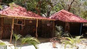 Two rustic huts with thatched roofs, surrounded by palm trees and a sandy ground. - Bidi Badu Zanzibar Village - Hostel (Diani Beach)