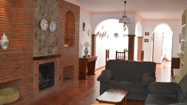 A living room with a brick fireplace, a sofa, and a dining area with a table and chairs. - Villa Remedios, whole house located in rural environment. (Málaga)