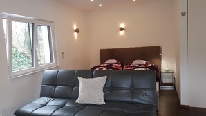 A modern room with a leather sofa, a bed with floral bedding, and two wall-mounted lights. - Luxus Apartment Zaubersee (Bergisch Gladbach)
