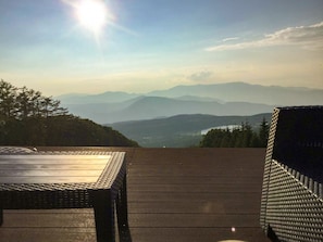 Een houten terras met een tafel en een rieten stoel, met uitzicht op een bergachtig landschap.