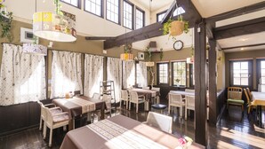 A dining area with tables and chairs, large windows, and hanging plants. - Pension Wildflowers (Tateshina)