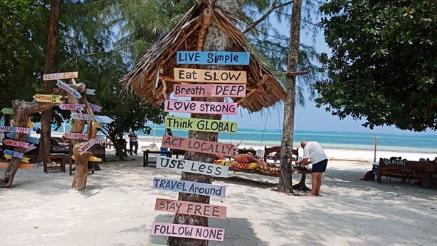 Una playa con un cartel que enumera varias frases relacionadas con viajes.