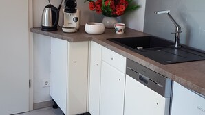 A modern kitchen with white cabinets, a countertop with a kettle, coffee maker, and a vase of flowers. - Luxusapartment Steinbreche (Bergisch Gladbach)