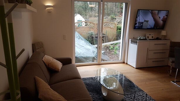A living room with a brown sofa, a glass coffee table, and a TV on the wall. - Luxusapartment Steinbreche (Bergisch Gladbach)