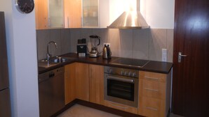 A modern kitchen with wooden cabinets, a stainless steel range hood, a built-in oven, a dishwasher, and a coffee maker. - Großzügiges Zweiraumapartment Troisdorf (Troisdorf)