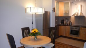 A dining area with a round table, four chairs, a vase with flowers, a lamp, and a kitchen in the background. - Großzügiges Zweiraumapartment Troisdorf (Troisdorf)