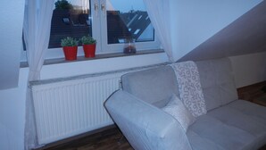 A room with a white radiator, a grey sofa, and a window with red potted plants. - Großzügiges Zweiraumapartment Troisdorf (Troisdorf)