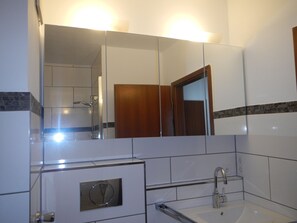A bathroom with a mirror, sink, and shower. - Großzügiges Zweiraumapartment Troisdorf (Troisdorf)