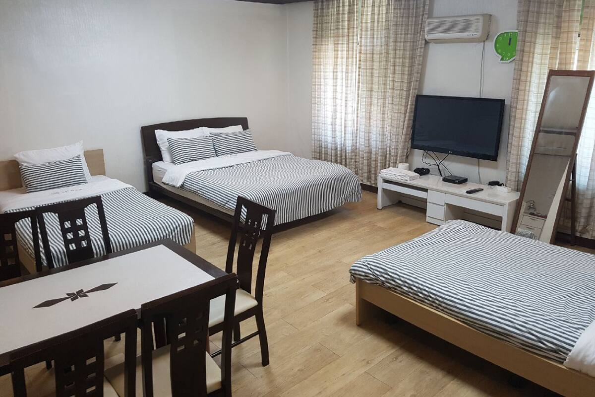 A hotel room with two single beds, a desk with a chair, a television, and an air conditioning unit.