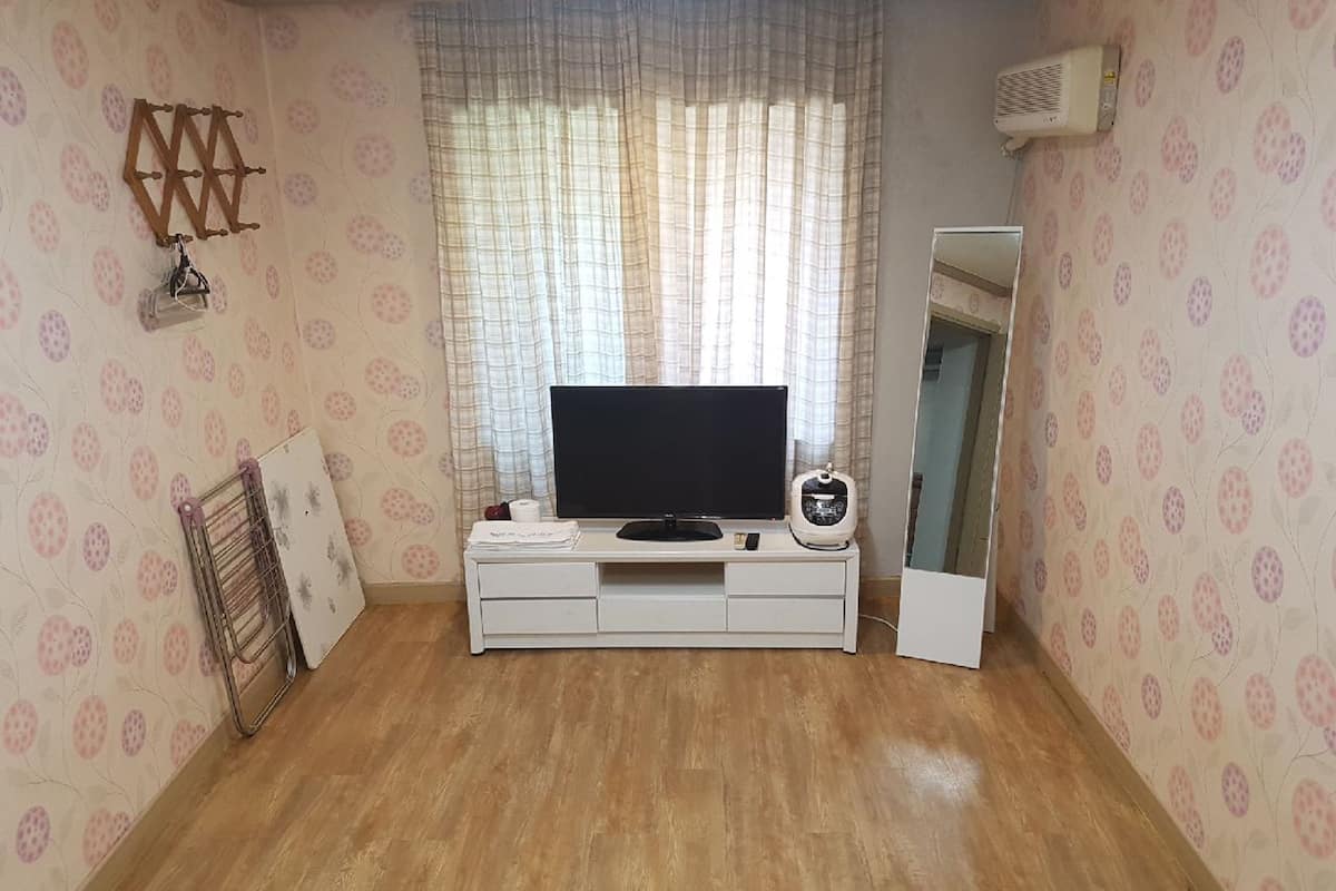 A room with a TV on a white cabinet, a mirror, and patterned wallpaper.