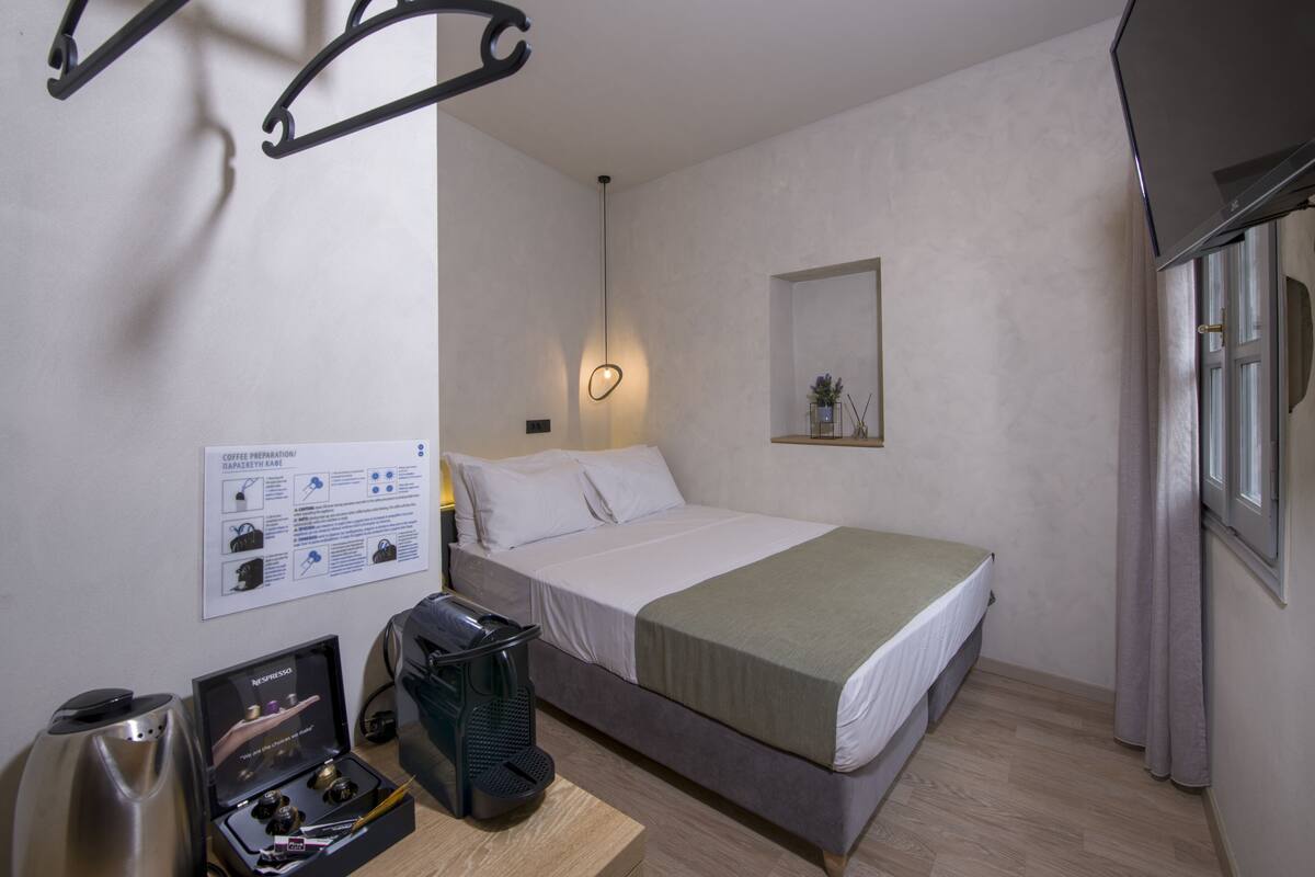 A hotel room with a bed, a coffee machine, a mirror, and a window.