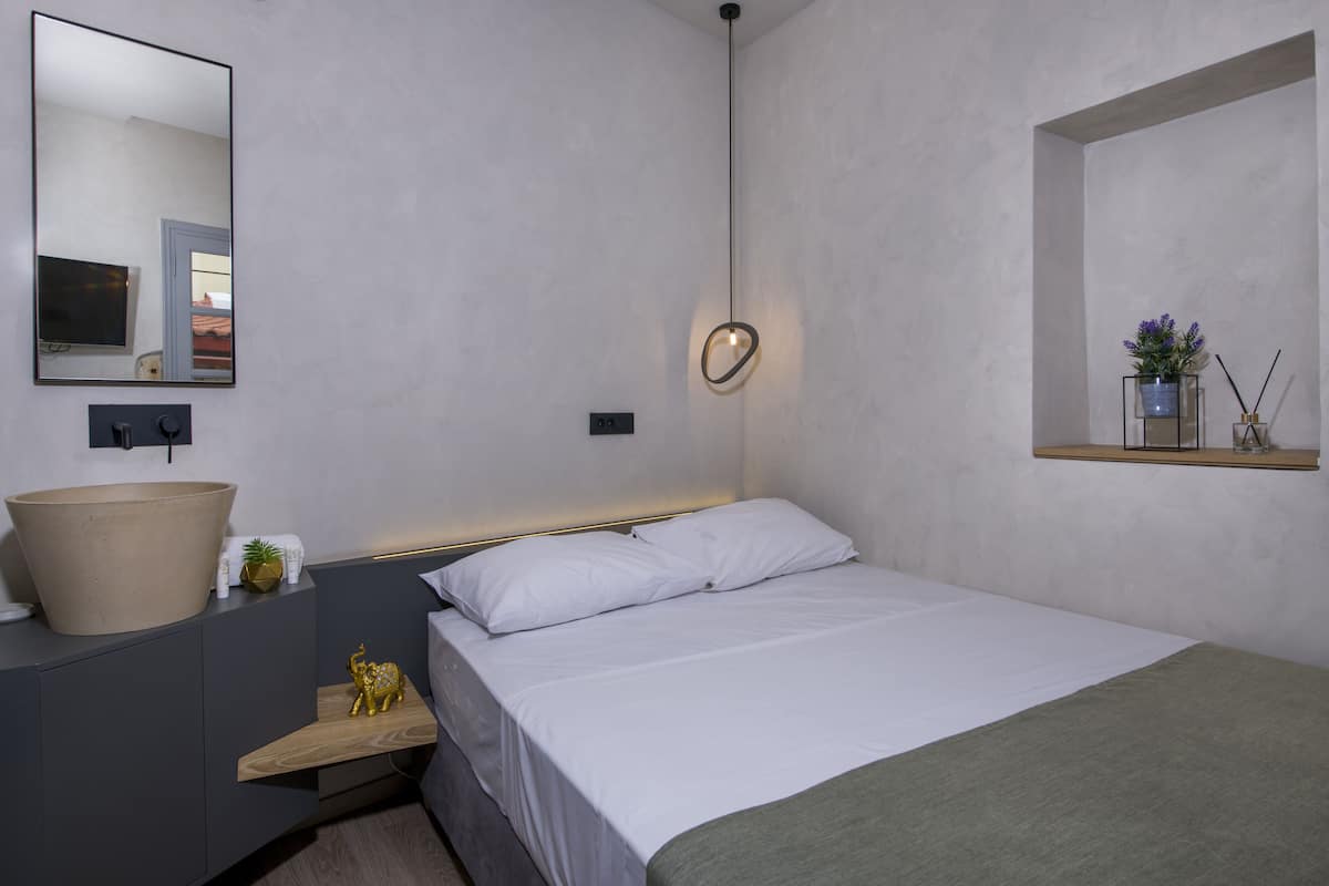 A modern bedroom with a large round mirror, a bedside table with a bowl sink, a small elephant figurine, and a bedside lamp.