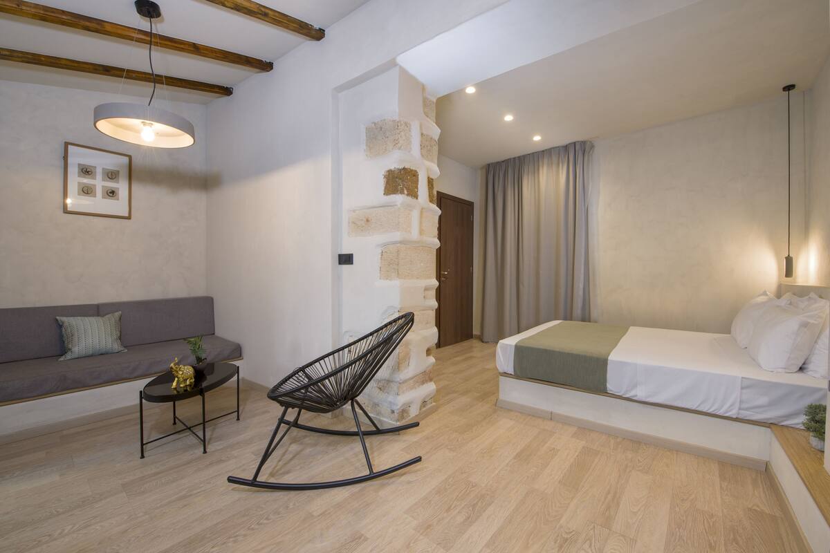 A modern living room with a sofa, a rocking chair, a coffee table, and a staircase leading to another room.
