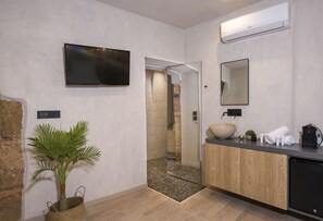 Une salle de bain moderne avec un grand miroir, un lavabo en forme de cuvette, un téléviseur fixé au mur et une plante en pot.